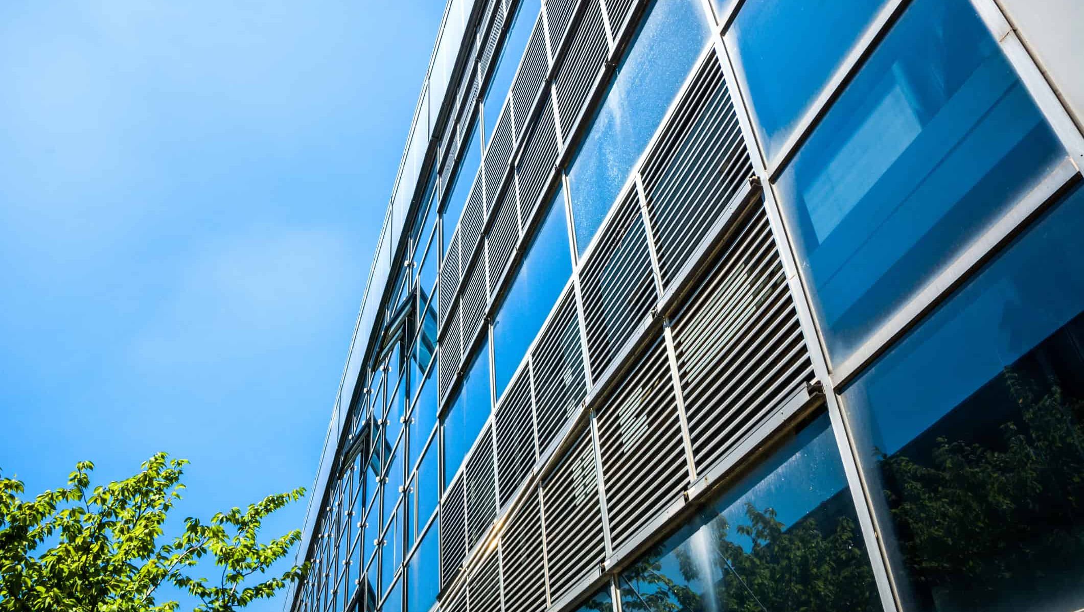 Moderne kontorbygg med glassfasade, solskjerming og reflekser i store vindusflater.