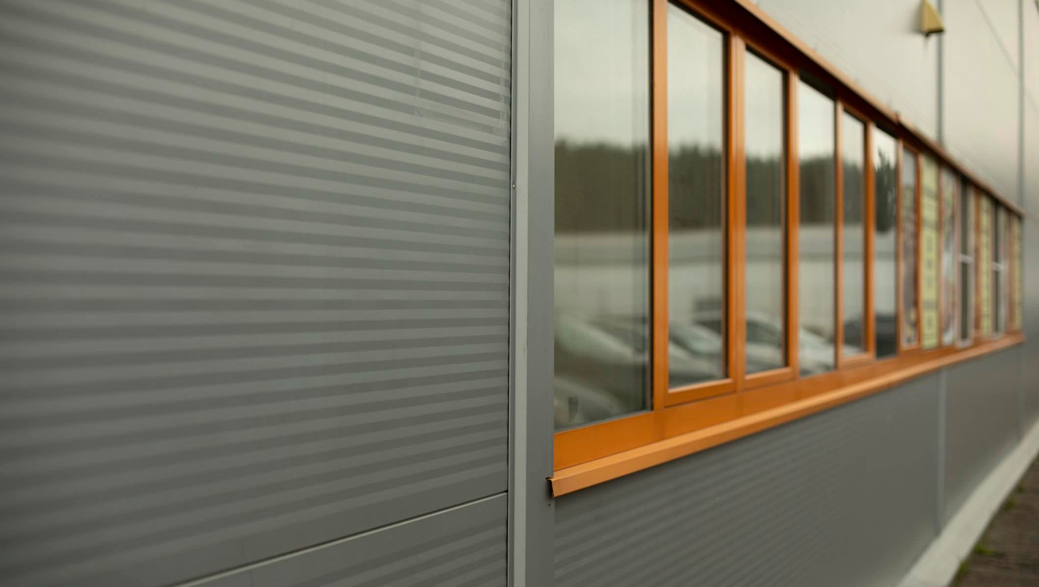 Fasade med grå sandwichpaneler og vindusbånd med oransje aluminiumsrammer.